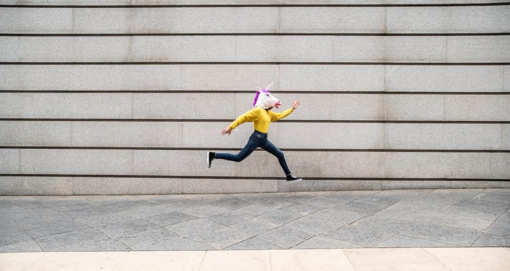 Female wearing vibrant unicorn mask jumping against wall